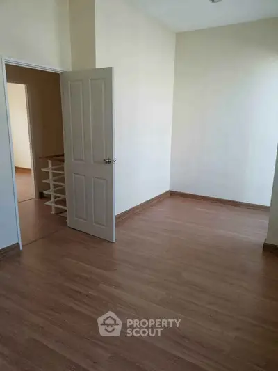 Spacious empty room with wooden flooring and open door leading to another room.