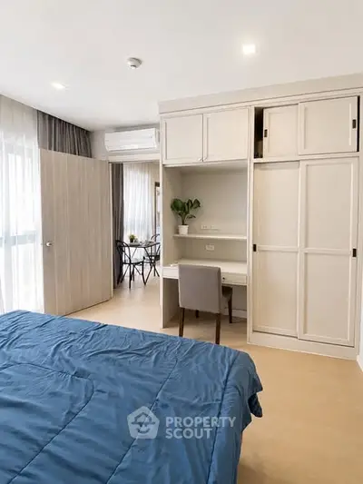 Modern bedroom with built-in storage and cozy workspace, featuring natural light and elegant decor.