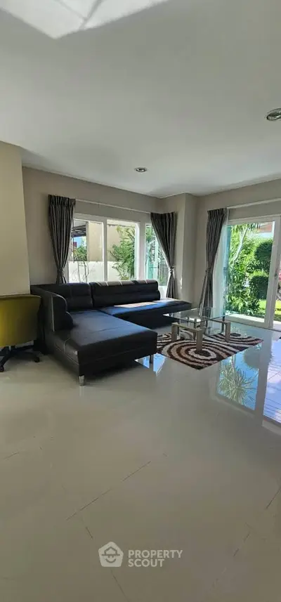 Spacious living room with modern black sofa and large windows overlooking garden