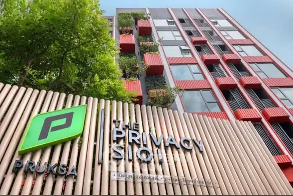 Modern apartment building with unique red facade and lush greenery.