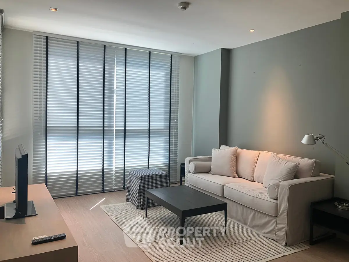Modern living room with stylish sofa and large windows with blinds
