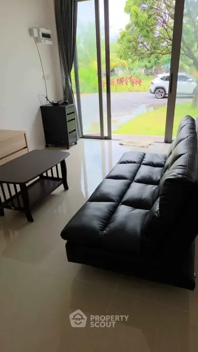 Modern living room with sleek black sofa and large glass doors opening to a lush garden view.