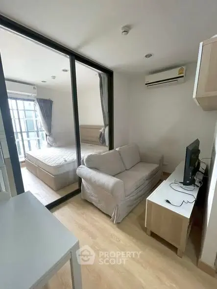 Modern compact living room with glass partition to bedroom, featuring cozy sofa and sleek TV setup.