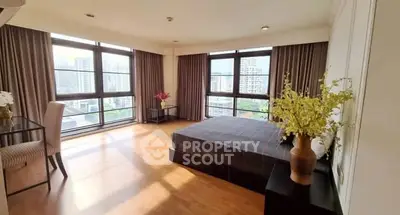 Spacious bedroom with large windows and city view, featuring elegant decor and natural light.