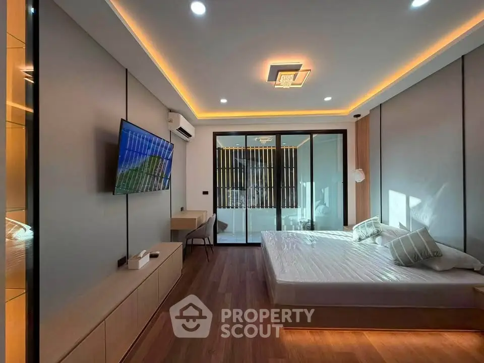 Modern bedroom with sleek design, featuring a mounted TV, ambient lighting, and large windows for natural light.
