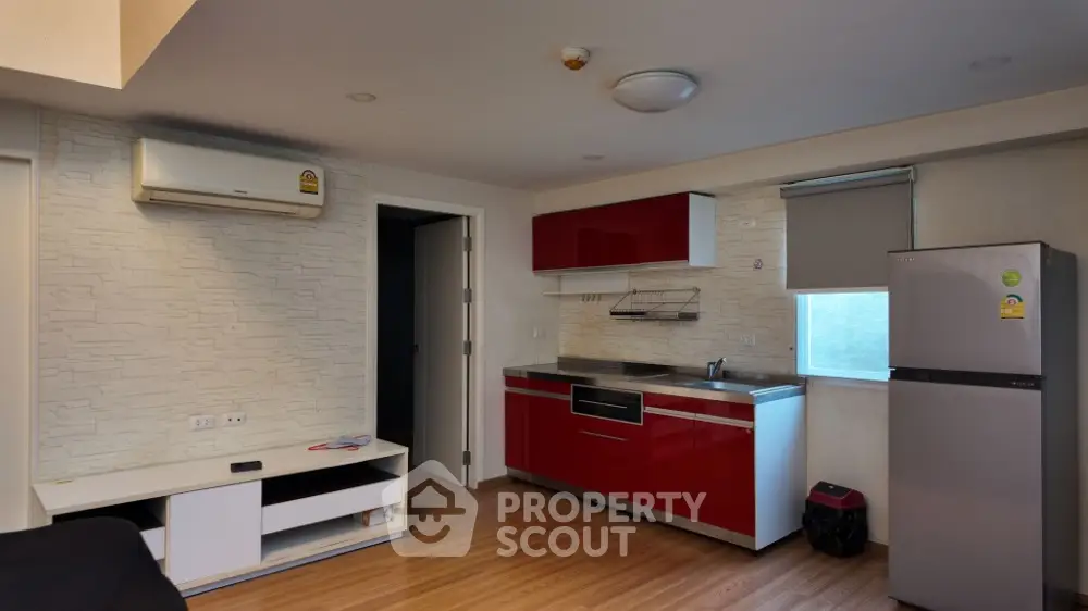 Modern kitchen with red cabinets and stainless steel appliances in a cozy apartment.