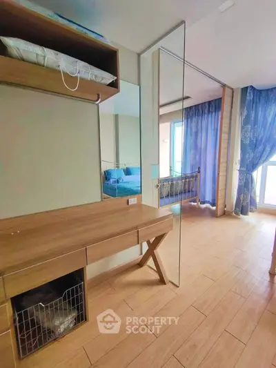 Spacious bedroom with wooden flooring and large mirror, featuring elegant blue curtains and a cozy bed.