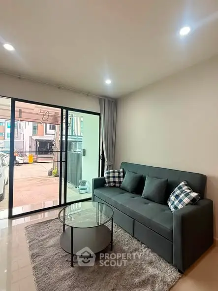 Modern living room with sleek sofa and glass coffee table, featuring large windows for natural light.
