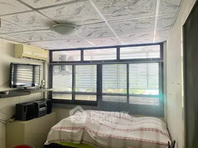 Cozy bedroom with large windows and modern ceiling design, featuring a wall-mounted TV and stereo system.
