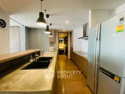 Modern kitchen with sleek design, featuring a large fridge, stylish lighting, and wooden flooring.