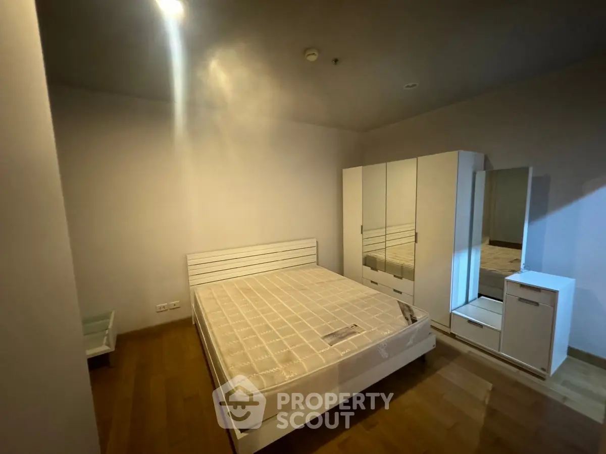 Spacious bedroom with wooden flooring and modern white furniture.