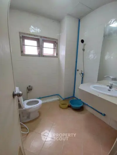 Compact bathroom with tiled floor, toilet, and sink, featuring basic plumbing and small window.