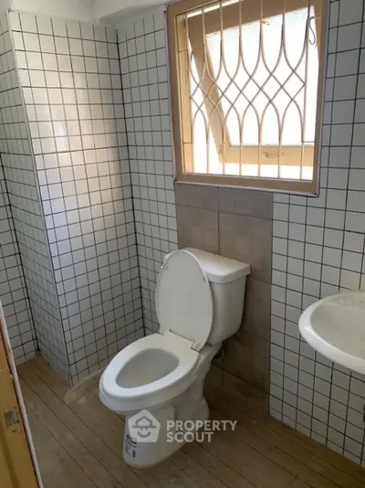 Compact bathroom with tiled walls and window, featuring a toilet and sink.