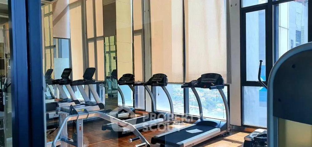 Modern gym with treadmills and large windows offering city views in luxury building.