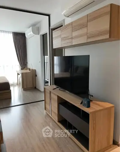 Modern living room with sleek wooden furniture and large TV, featuring a cozy bedroom view.
