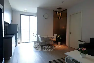 Modern living room with open kitchen and dining area, featuring sleek furniture and natural light.