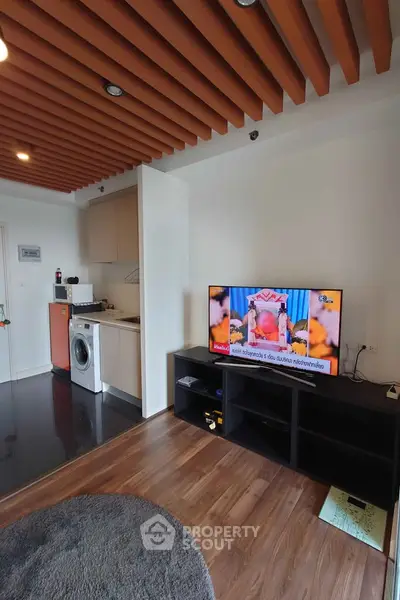Modern living room with stylish ceiling, TV, and compact kitchen area.
