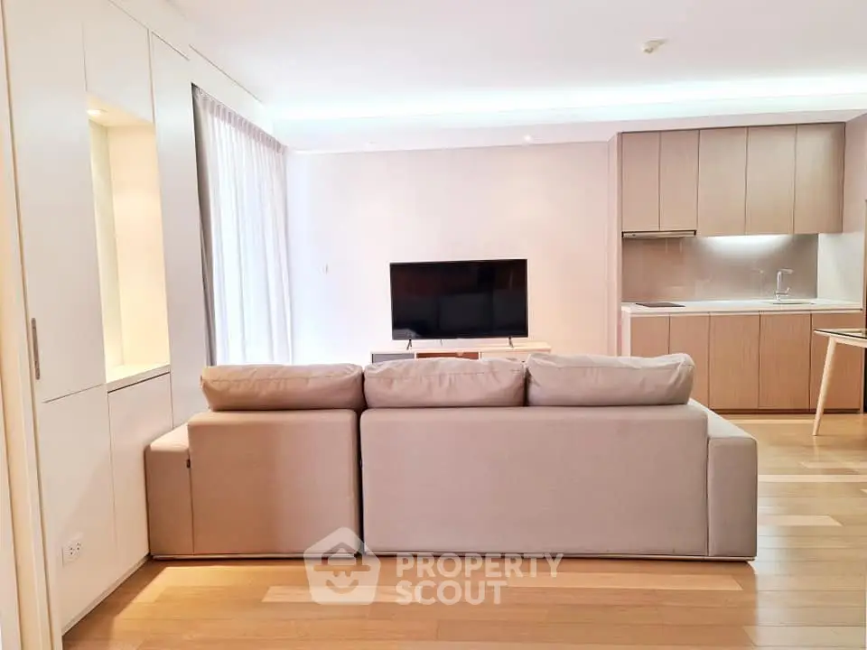 Modern living room with open kitchen, featuring sleek furniture and natural light.