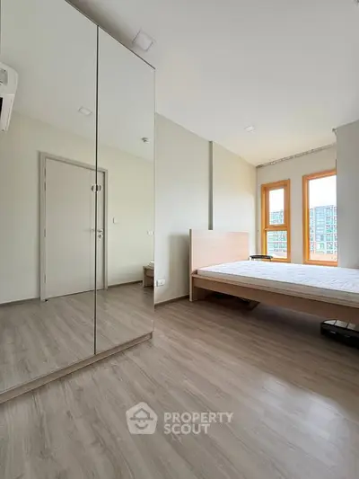 Modern bedroom with mirrored wardrobe and large windows offering natural light.