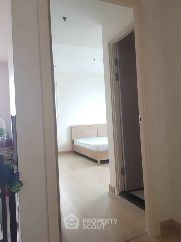 Bright bedroom with minimalist wooden bed and open doorway view.
