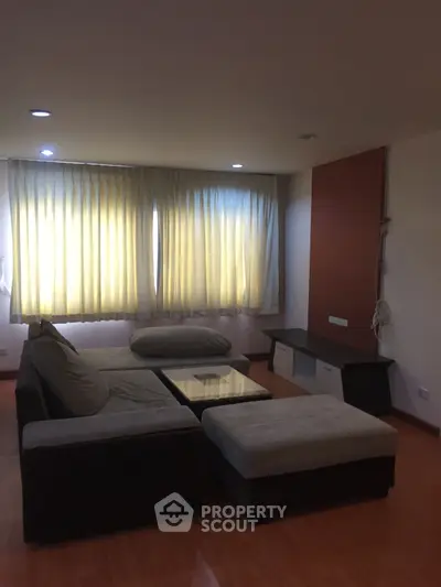 Spacious living room with cozy sectional sofa and large windows with curtains.