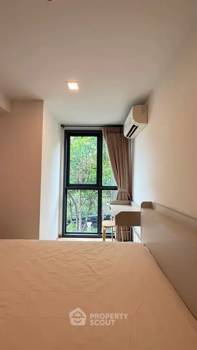 Modern bedroom with large window and air conditioning, offering a serene view of greenery.