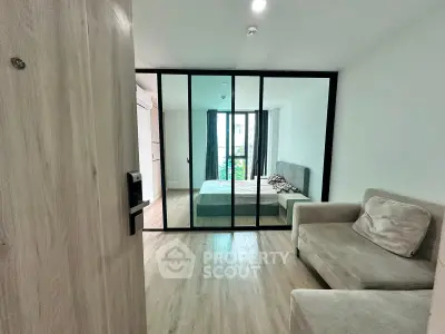 Modern bedroom with glass partition and cozy seating area, featuring natural light and minimalist design.