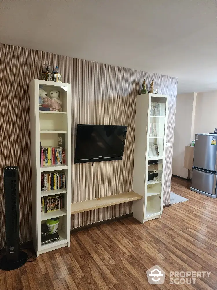 Spacious living room with modern wood flooring, stylish wallpaper, and built-in shelving units flanking a sleek flat-screen TV.