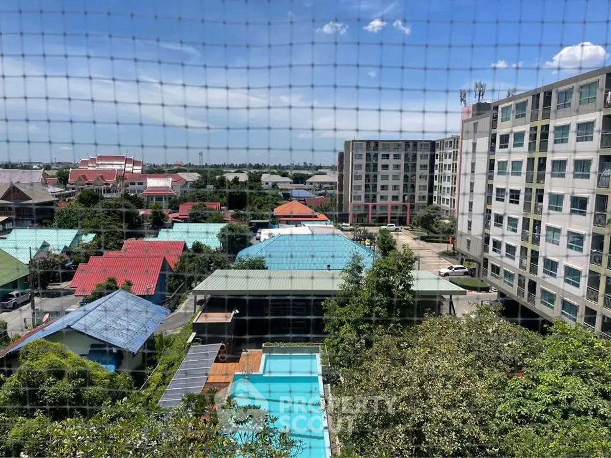 Stunning aerial view of residential buildings with lush greenery and a sparkling pool under a clear blue sky.