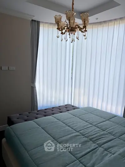 Luxurious bedroom with elegant chandelier and large windows with sheer curtains.