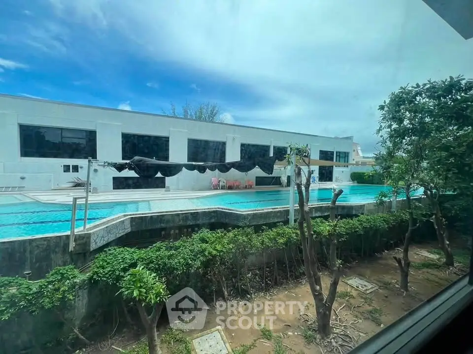 Luxurious poolside view of modern building with lush greenery and clear blue sky.