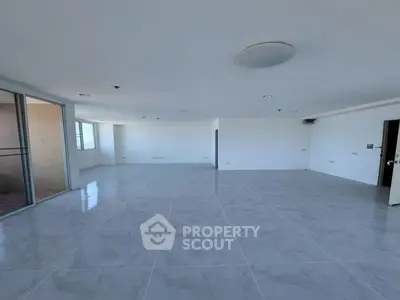 Spacious empty living room with large windows and modern tile flooring.