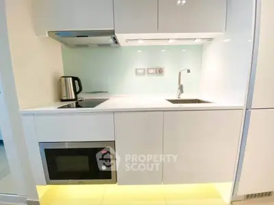 Modern compact kitchen with sleek white cabinetry and built-in appliances.