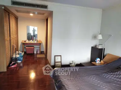 Spacious bedroom with wooden flooring and cozy decor, featuring a dressing area and ample storage space.