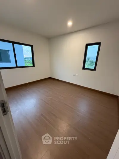 Spacious empty room with wooden flooring and two windows offering natural light.