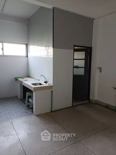 Spacious kitchen area with tiled walls and large window, ideal for renovation.