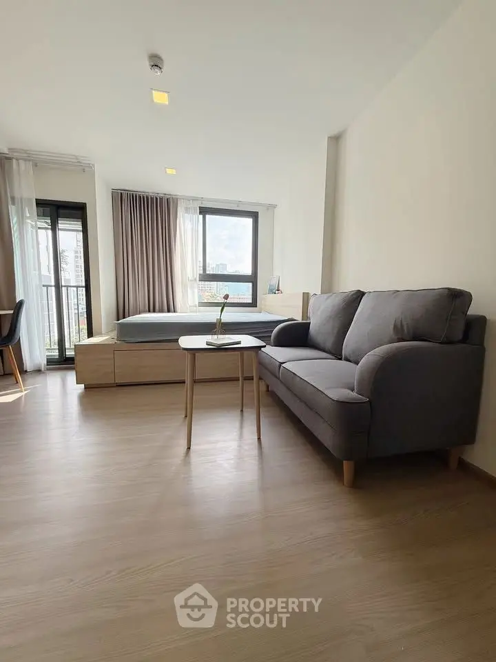 Modern studio apartment with cozy living area and large windows offering natural light.