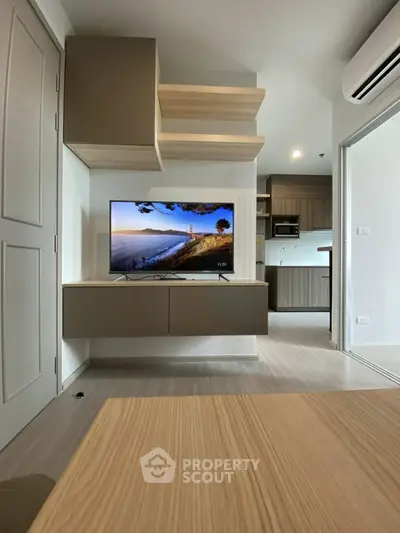 Modern living room with wall-mounted TV and open kitchen layout in stylish apartment.