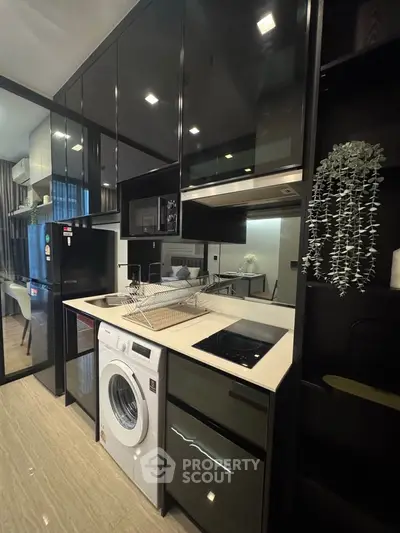 Modern kitchen with sleek black cabinets, built-in appliances, and washing machine in a compact layout.