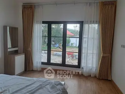 Cozy bedroom with large window and elegant curtains overlooking garden view.