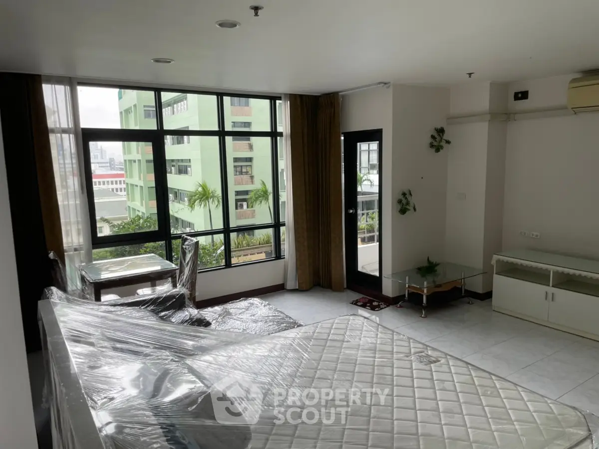Spacious living room with large windows and city view, featuring modern furniture and natural light.
