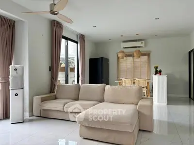 Spacious modern living room with beige sectional sofa and dining area, featuring large windows and elegant decor.