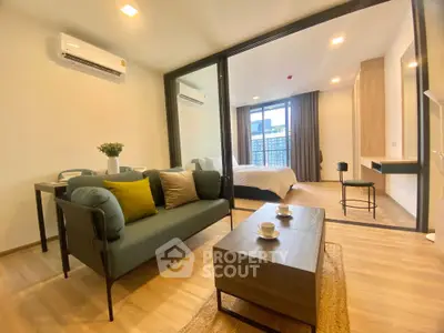 Modern open-plan living room with stylish furniture and a view into a cozy bedroom.