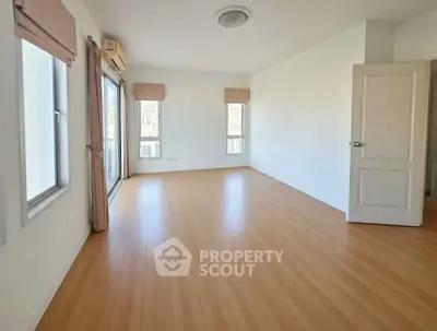 Spacious empty room with wooden flooring and large windows, perfect for customization.