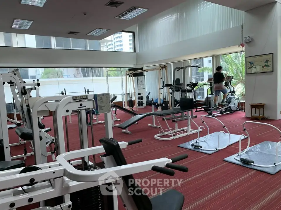 Spacious gym with modern fitness equipment and large windows in a residential building.