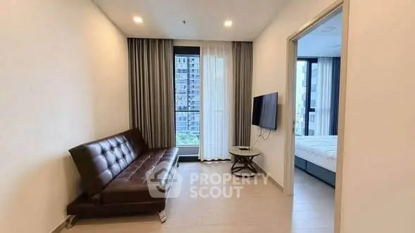 Modern living room with sleek sofa and wall-mounted TV, adjacent to a bright bedroom with city view.