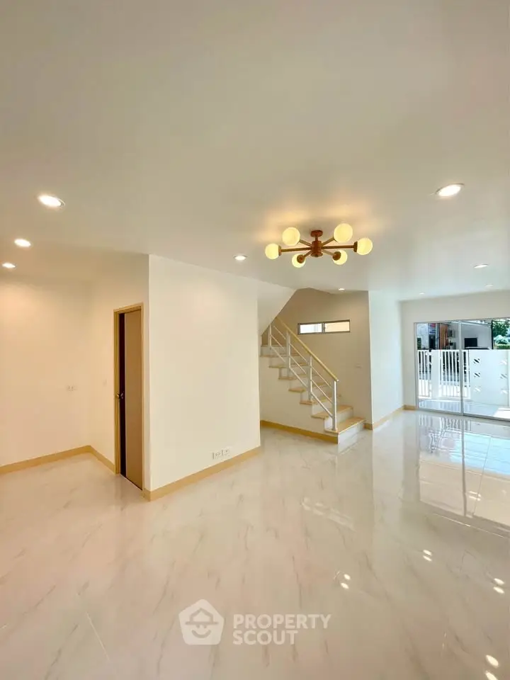 Spacious modern living room with elegant lighting and staircase, perfect for family gatherings.