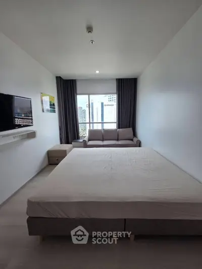 Spacious modern bedroom with large window and city view, featuring a cozy sofa and wall-mounted TV.