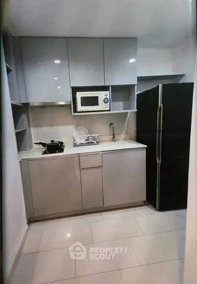 Modern kitchen with sleek cabinetry, microwave, and large fridge in a compact layout.