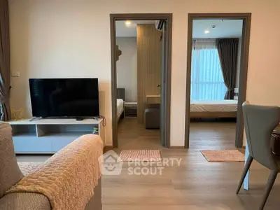 Modern apartment living room with TV, cozy sofa, and view into two bedrooms.